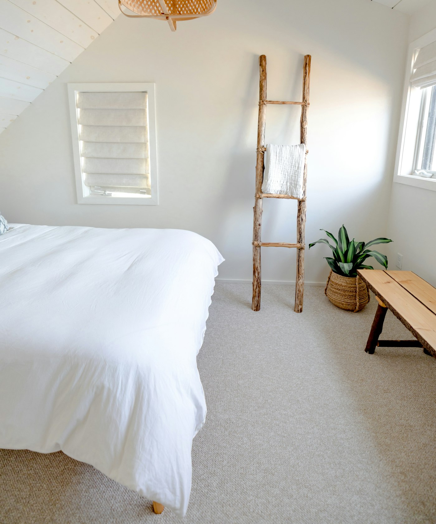 A white-linened bed in a light-filled room with a wooden ladder against the wall