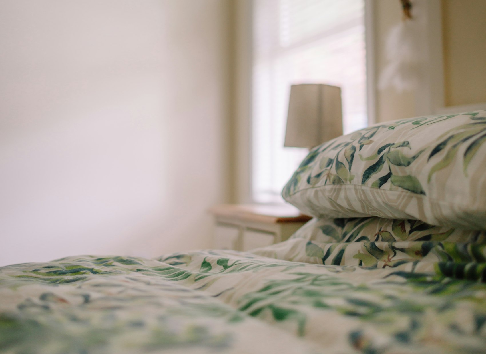 The Garden Room: a bed in green leaf-print linen in a pale room